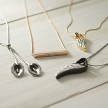 Various cremation necklaces with unique pendants on a light wooden surface